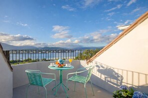 Un balcon avec une table et des chaises, donnant sur un plan d’eau et des montagnes.