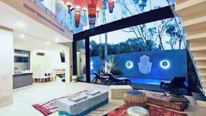A modern interior with a large glass wall, a seating area with cushions, and a view of trees outside. - Tulum Dream Villa: Designer Luxury Near The Beach (Tulum)