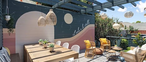 Eine Holzterrasse mit Tisch, Stühlen, einer Pergola und hängenden Lampen.