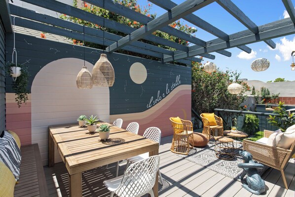 A wooden deck with a table and chairs, a pergola, and hanging lights.