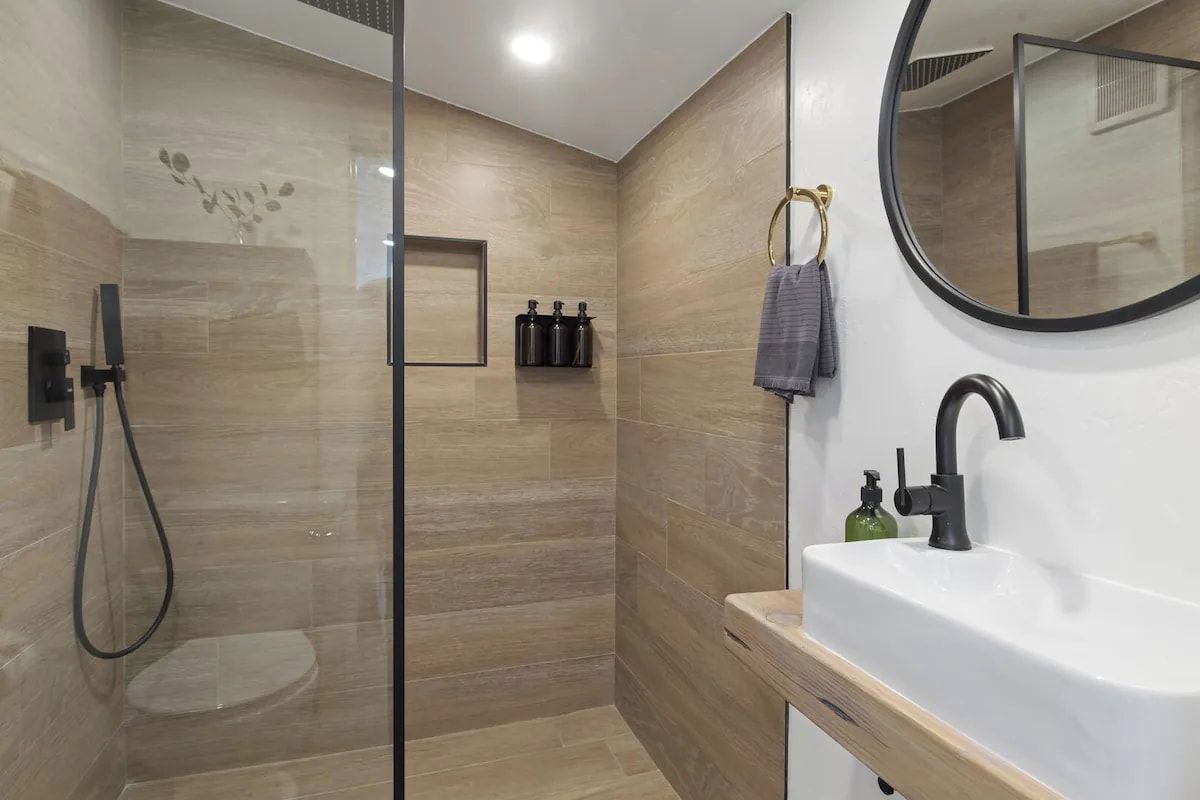 A modern bathroom with a glass shower enclosure, a white sink, and a round mirror.