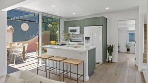 A modern kitchen with a central island, white cabinets, and a microwave. - 5BR (Sleeps 12!)  Downtown Little Italy Home w/ Outdoor Space (San Diego)