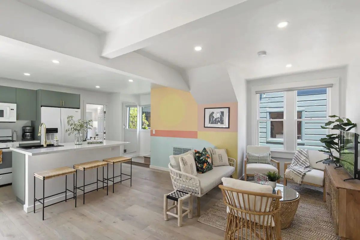 A modern kitchen with a central island, bar stools, and a seating area with a sofa and chairs.