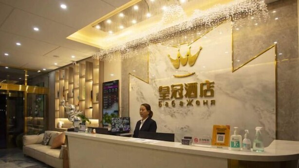 Un mostrador de recepción con el logotipo de una corona, una recepcionista y una pared de mármol.