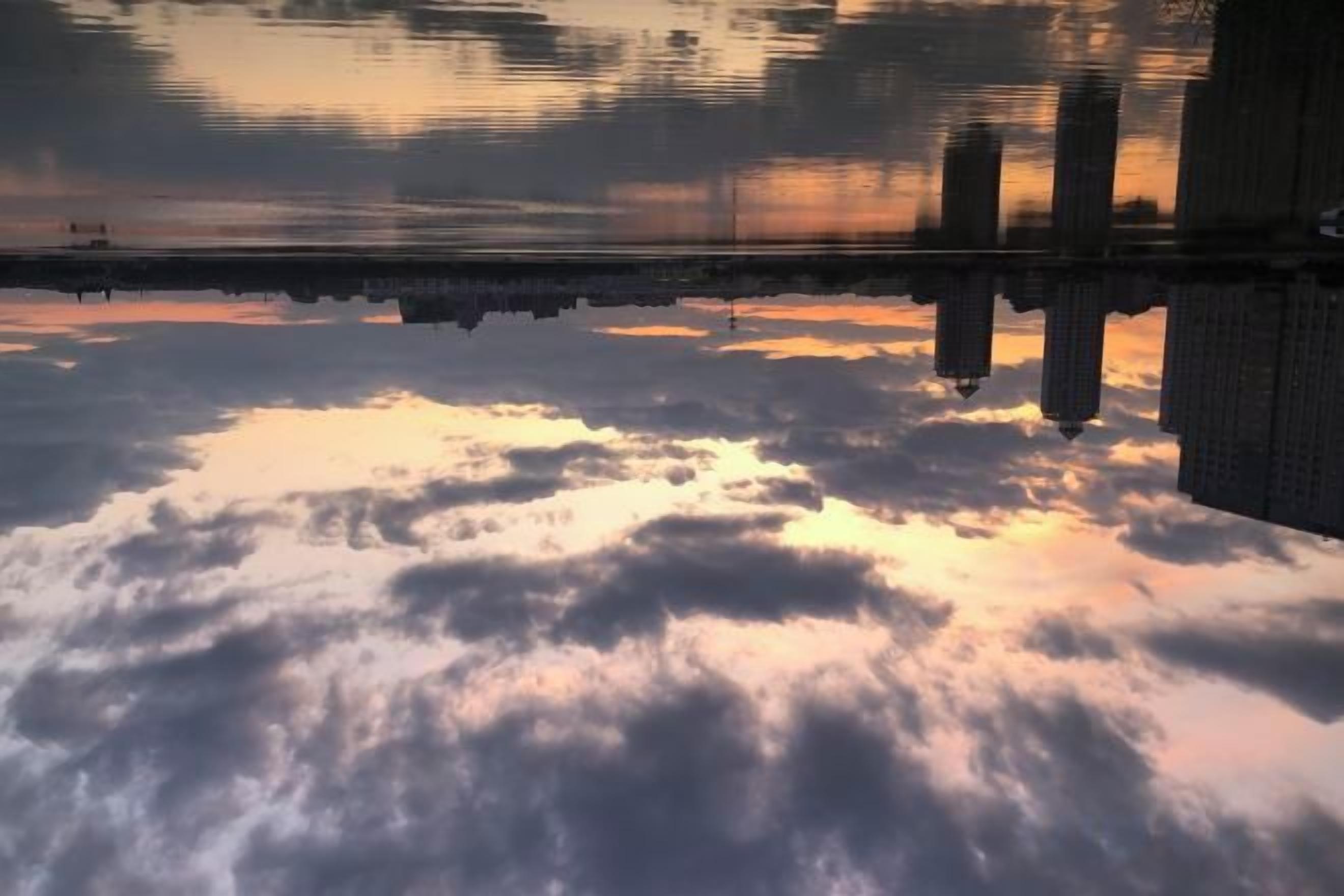 A reflection of clouds and buildings on a body of water.