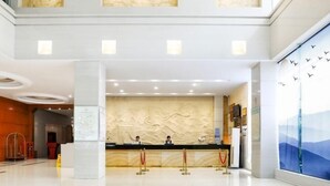 A hotel reception area with a modern design, featuring a reception desk, two staff members, and a large wall mural. - Holiday Villas Airport (Guangzhou Baiyun International Airport) (Guangzhou)