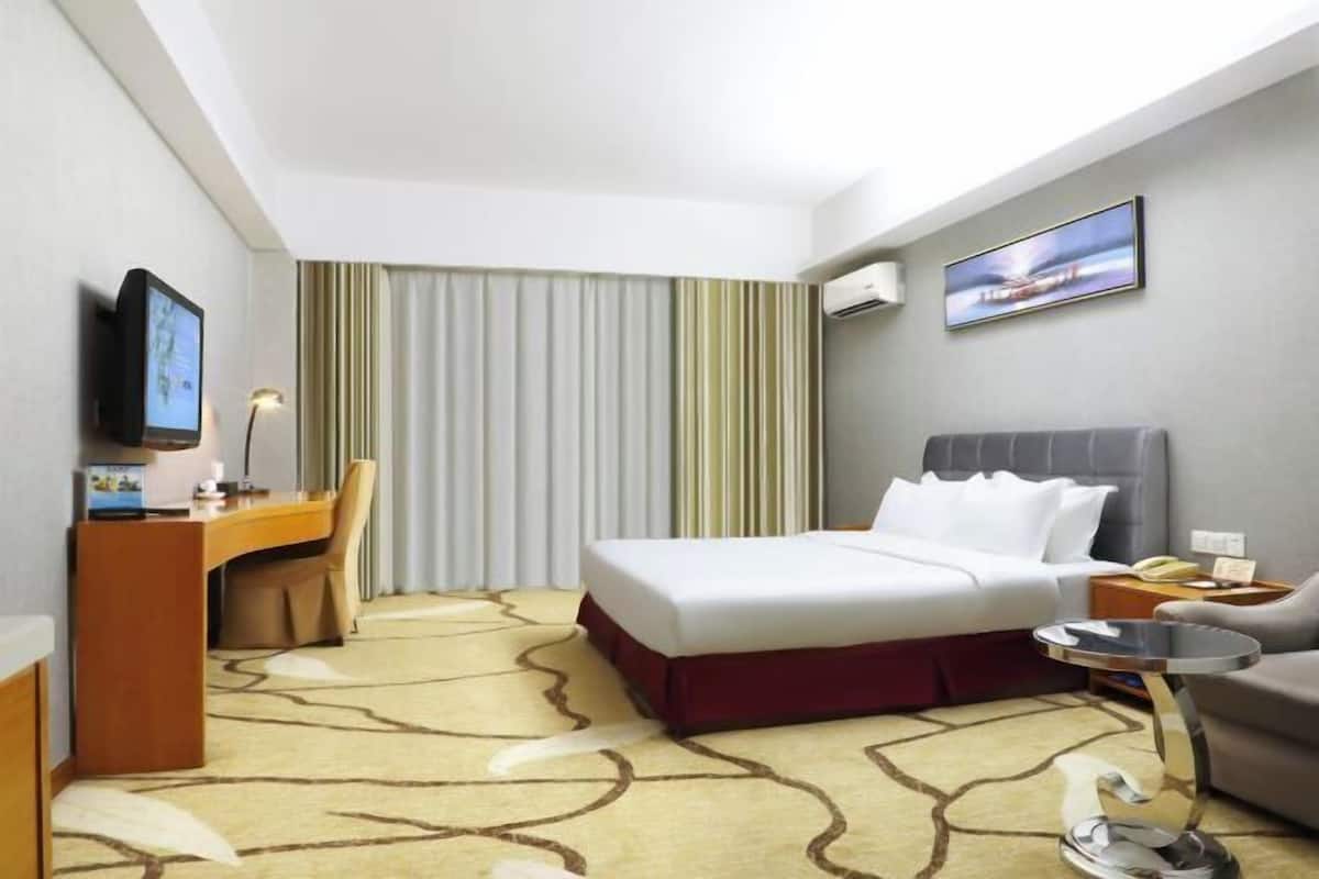 Une chambre d’hôtel équipée d’un lit, d’un bureau, d’une chaise, d’une télévision, d’une table de chevet et d’une lampe.
