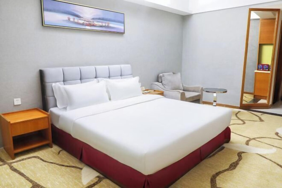 Een hotelkamer met een groot bed, een nachtkastje, een stoel, een tafeltje en een spiegel.