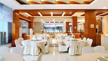 A hotel dining area with round tables, white chairs, and a modern ceiling design.