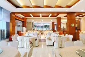 Un comedor de hotel con mesas redondas, sillas blancas y un diseño moderno en el techo.