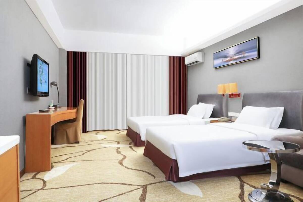 Une chambre d’hôtel avec deux lits, un bureau, une chaise, une télévision et un tableau au mur.