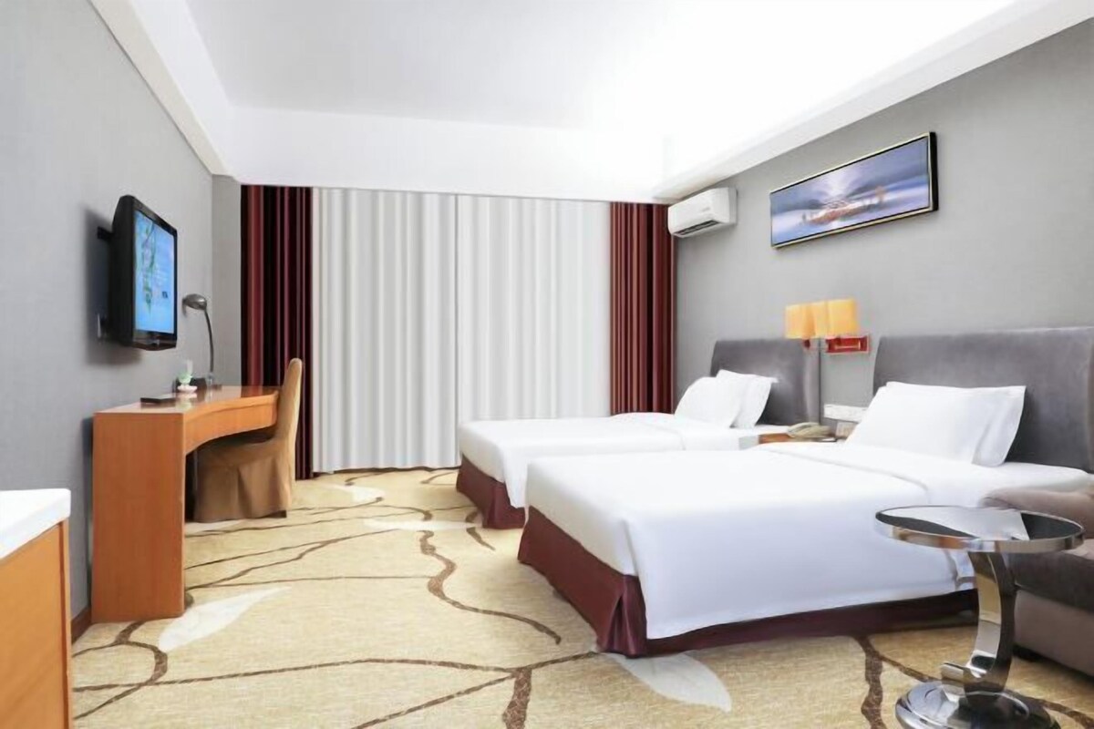 Een hotelkamer met twee bedden, een bureau, een stoel, een televisie en een schilderij aan de muur.