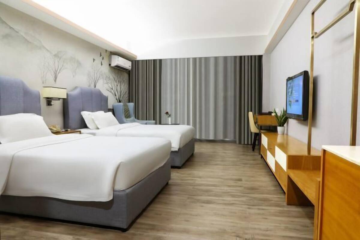 Une chambre d’hôtel avec deux lits, un bureau, une chaise, une télévision et une grande fenêtre avec des rideaux.
