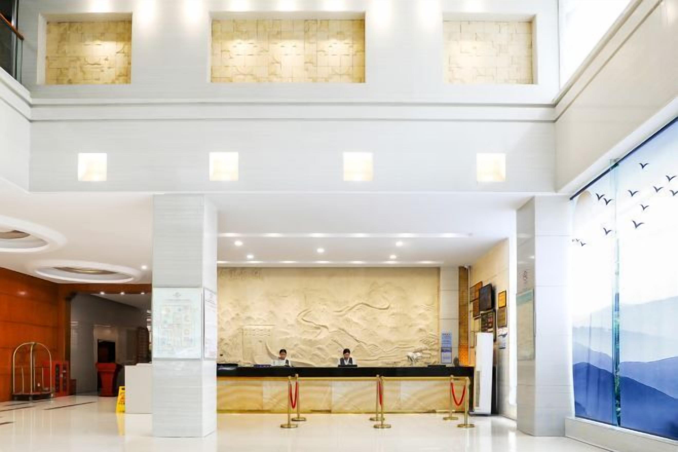 A hotel lobby with a reception desk, a large window with a view, and a modern architectural design.