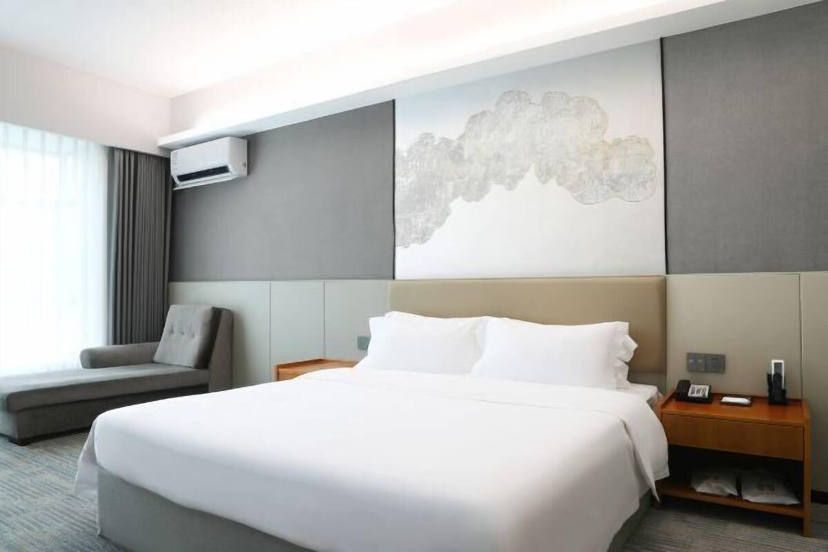 Une chambre d’hôtel moderne, dotée d’un grand lit, d’un canapé, d’une table de chevet et d’un climatiseur fixé au mur.