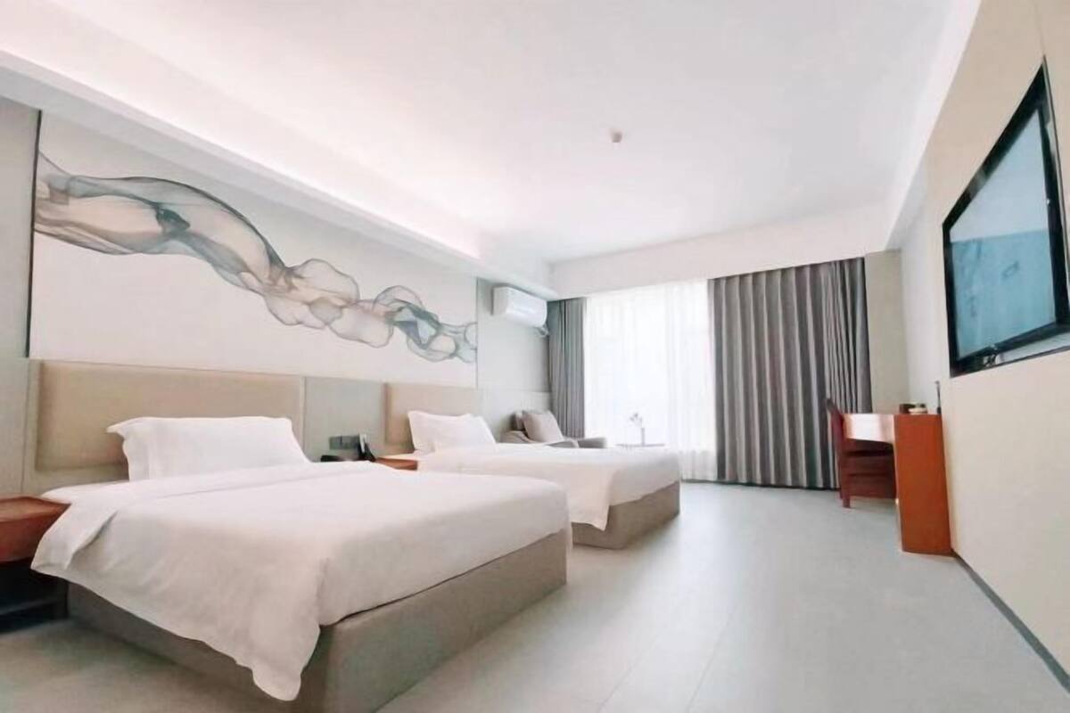 Une chambre d’hôtel moderne avec deux lits, une grande œuvre d’art au mur, un bureau et une télévision.