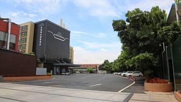 A hotel entrance with a black facade, a parking lot, and a street with parked cars.