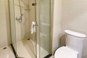 A bathroom with a glass shower enclosure, a white toilet, and a towel rack.