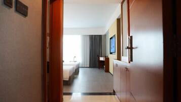 A hotel hallway leading to a room with a bed, a desk, and a television.