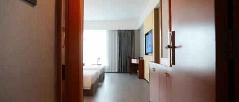 Un pasillo de hotel que conduce a una habitación con una cama, un escritorio y una televisión.