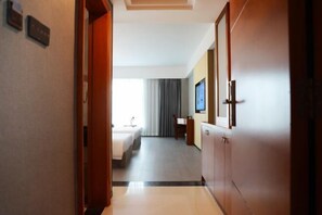 A hotel hallway leading to a room with a bed, a desk, and a television. - Holiday Villas Airport (Guangzhou Baiyun International Airport) (Guangzhou)