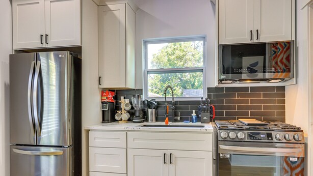 A modern kitchen with white cabinetry, a stainless steel refrigerator, a microwave, and a gas stove.