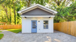 A small, single-story building with a blue door and windows, surrounded by a wooden fence and a brick pathway.