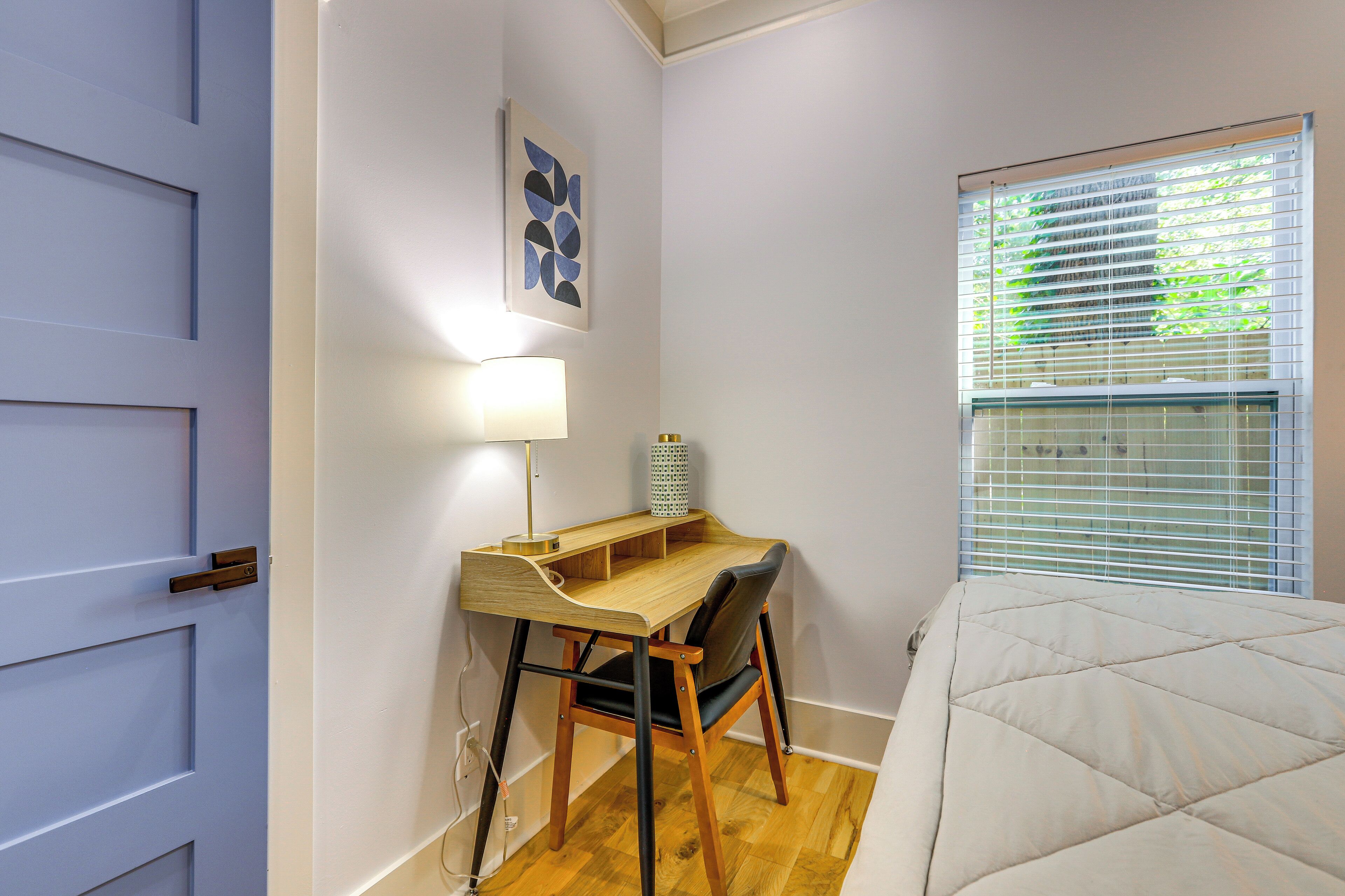 A bedroom with a bed, a desk with a chair, a lamp, and a window with blinds.