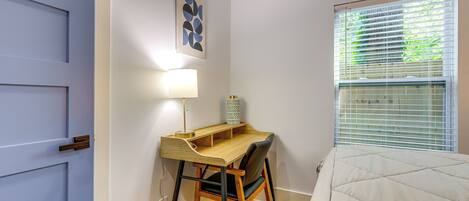 A bedroom with a bed, a desk with a chair, a lamp, and a window with blinds.