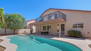 Una casa con piscina, un patio cubierto y un balcón de dos pisos.