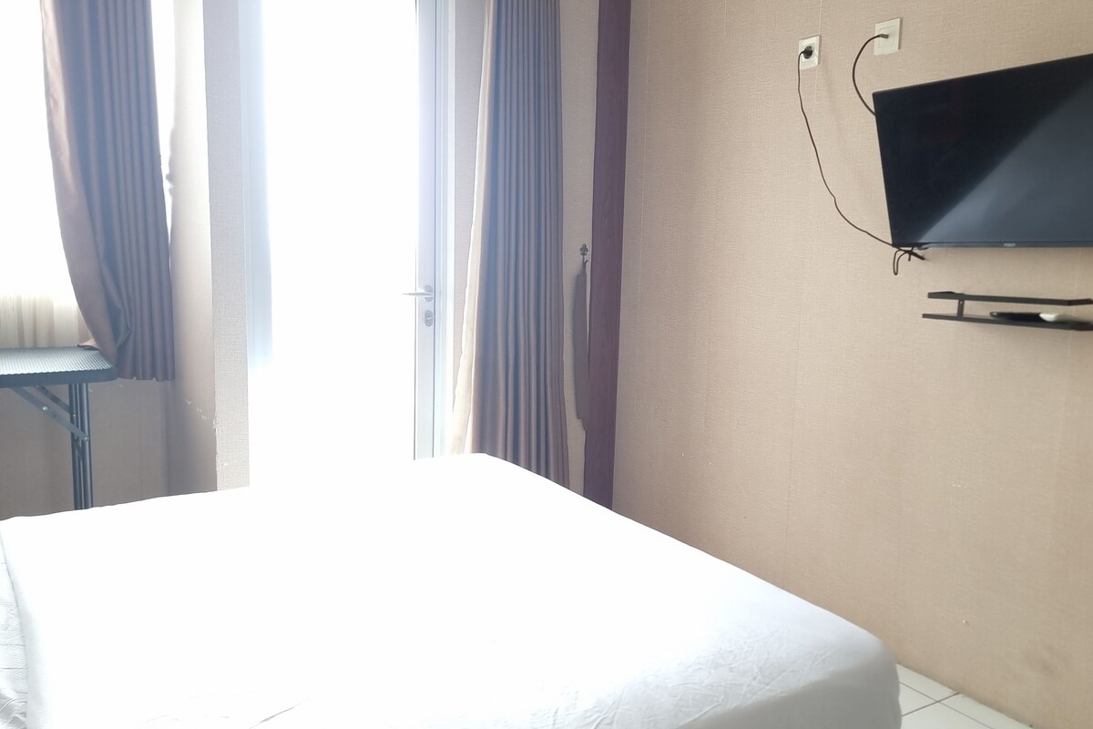 Une chambre d’hôtel avec un lit, un téléviseur fixé au mur et une fenêtre avec des rideaux.