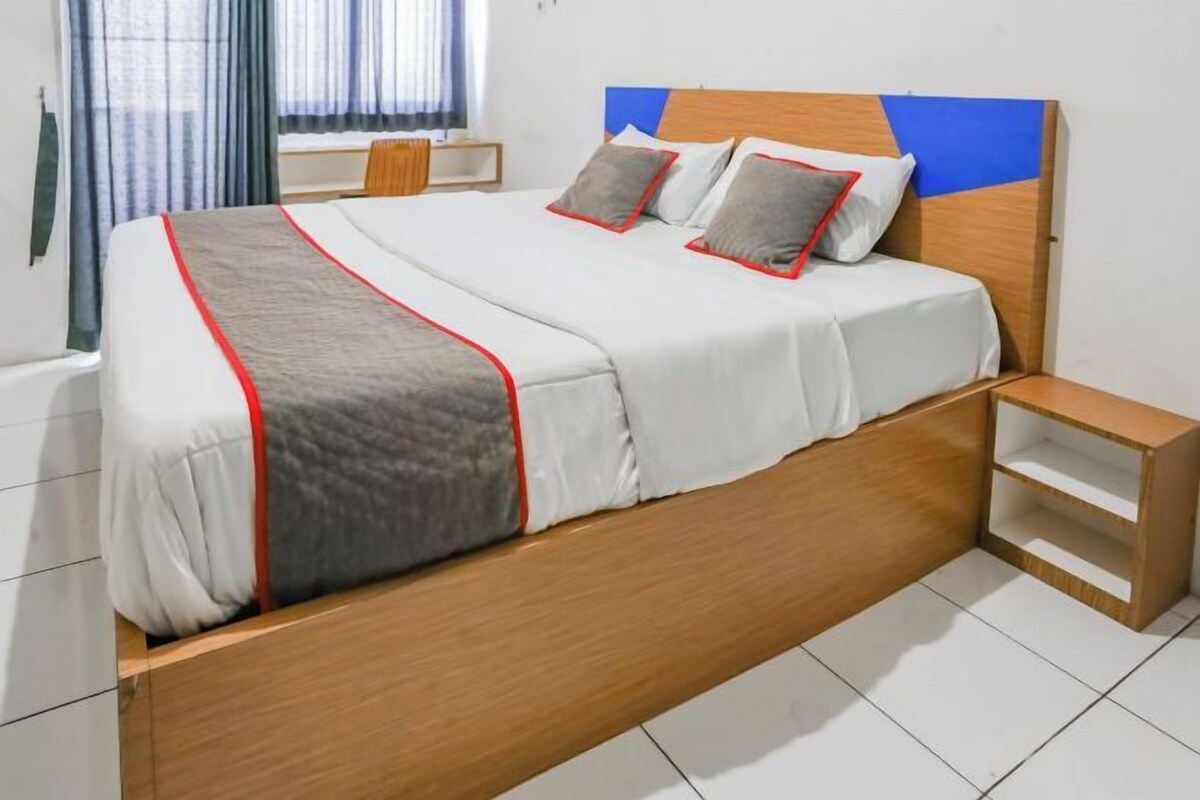 A neatly made bed with a wooden headboard, a bedside table, and a window with curtains.