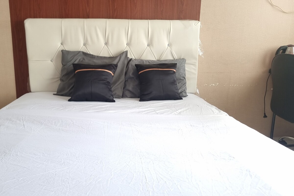 A bed with a white mattress, a tufted headboard, and two black pillows with orange trim.