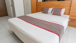 Un lit bien fait, avec une couverture blanche et rouge, une tête de lit en bois et deux oreillers.