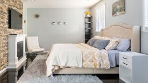 Un dormitorio con cama, una silla, televisor, chimenea y ventana con persianas.