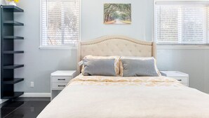 Un dormitorio con cama, dos mesitas de noche, un estante en la pared y una ventana con persianas.