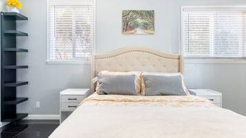 Une chambre à coucher comprenant un lit, deux tables de chevet, une étagère fixée au mur et une fenêtre avec des stores.