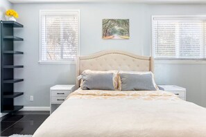 Un dormitorio con cama, dos mesitas de noche, un estante en la pared y una ventana con persianas.