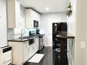 Une cuisine moderne avec des meubles blancs, un réfrigérateur noir, un four à micro-ondes et une cuisinière. On y trouve également un petit coin repas avec une table et des chaises.