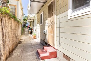 Uma estreita passagem entre dois edifícios, com um cercado de madeira de um lado e um prédio branco com um degrau vermelho que leva a uma porta do outro.