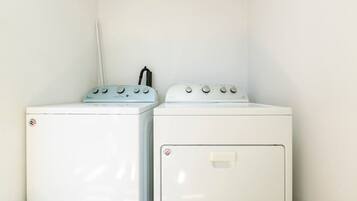Two white washing machines in a corner with a white wall.