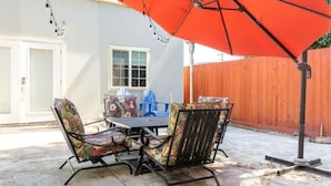 Un patio exterior con una mesa y sillas, un paraguas rojo y una valla de madera al fondo.