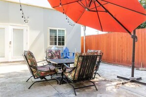 Un patio exterior con una mesa y sillas, un paraguas rojo y una valla de madera al fondo.