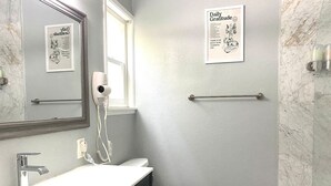 Un baño con un lavamanos blanco, un espejo, un perchero, un inodoro y una cita inspiradora enmarcada en la pared.