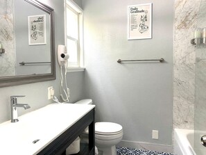 Un baño con un lavamanos blanco, un espejo, un perchero, un inodoro y una cita inspiradora enmarcada en la pared.