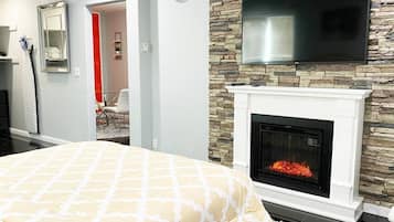 A bedroom with a fireplace, a bed with a patterned bedspread, a clock on the wall, and a television mounted above the fireplace.