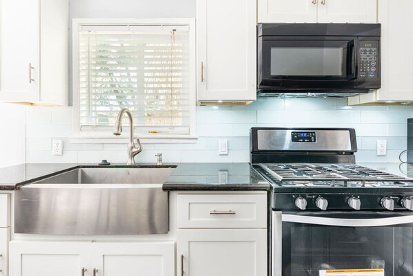A kitchen with white cabinets, a stainless steel sink, a black microwave, and a gas stove.