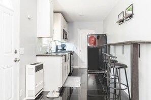 Cozinha compacta com armários brancos, micro-ondas embutido, geladeira e área de bar com banquetas.