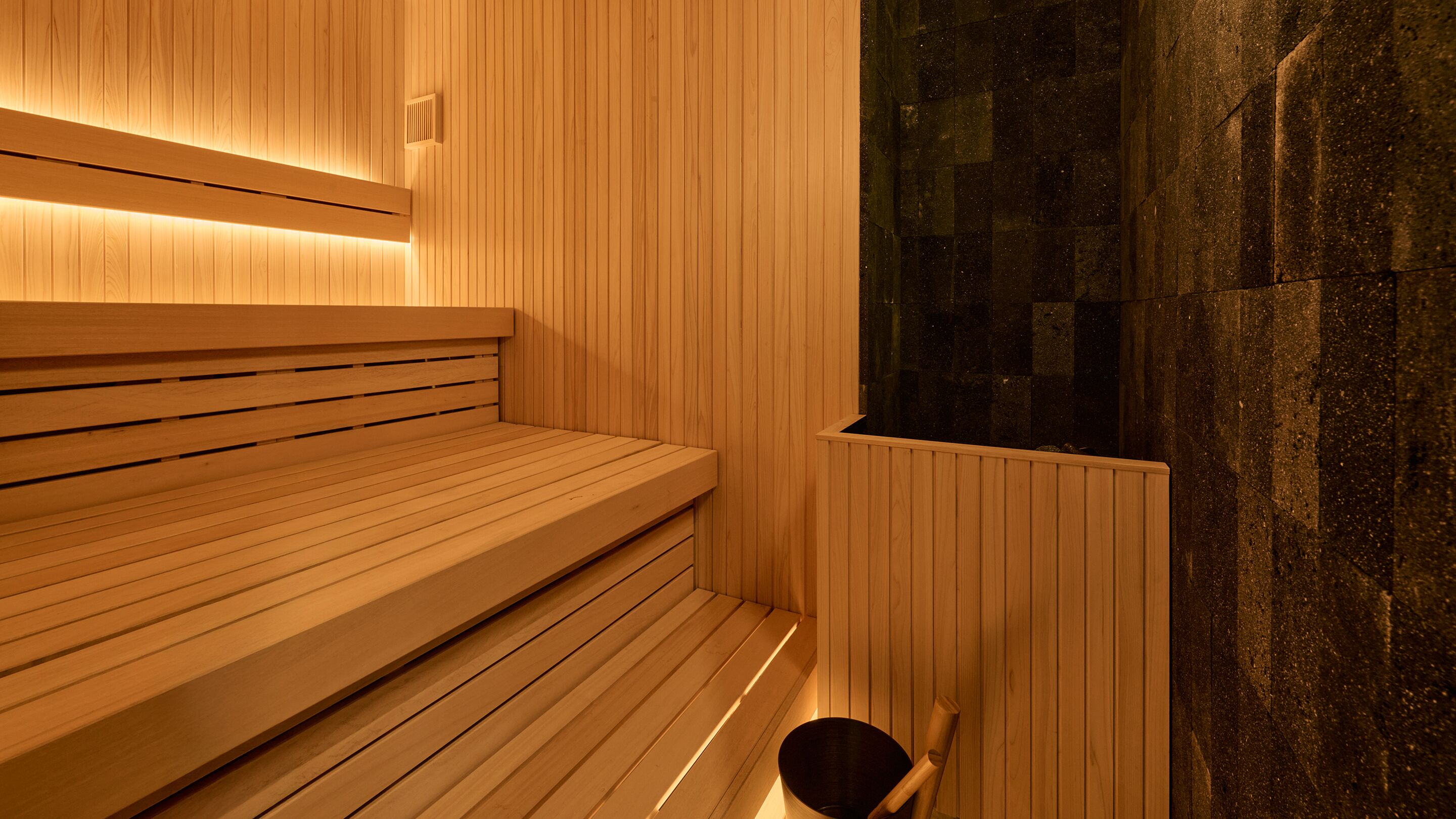 A wooden sauna with benches and a stone wall.