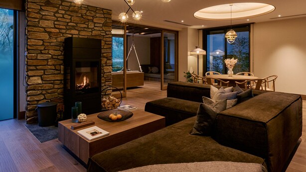 A modern living room with a stone fireplace, a dining area with a table and chairs, and a large window with a view of trees. - GLAMDAY STYLE HOTEL SUITE YAMANOFUMOTO (Karuizawa)